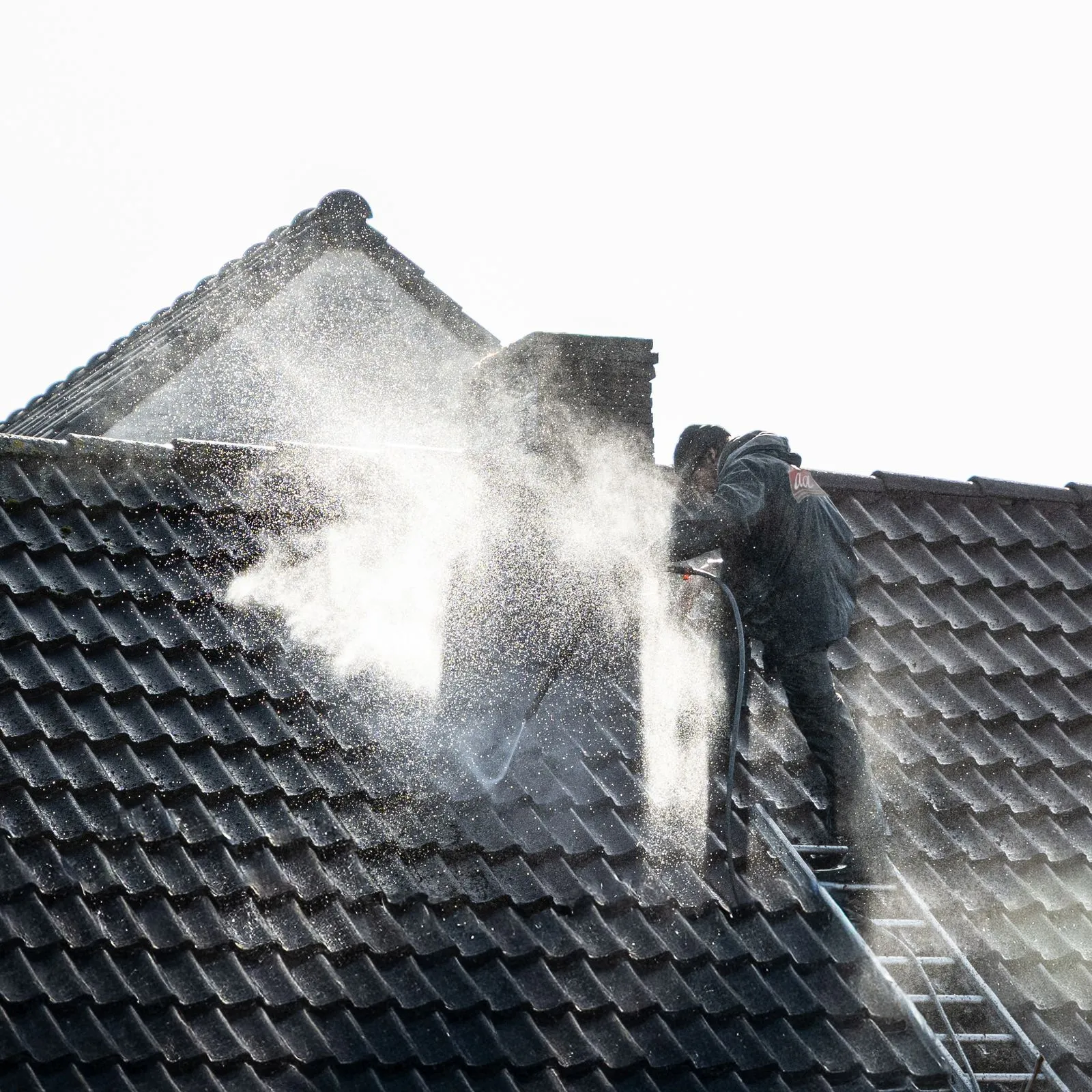 A worker cleaning grime and buildup from roof tiles