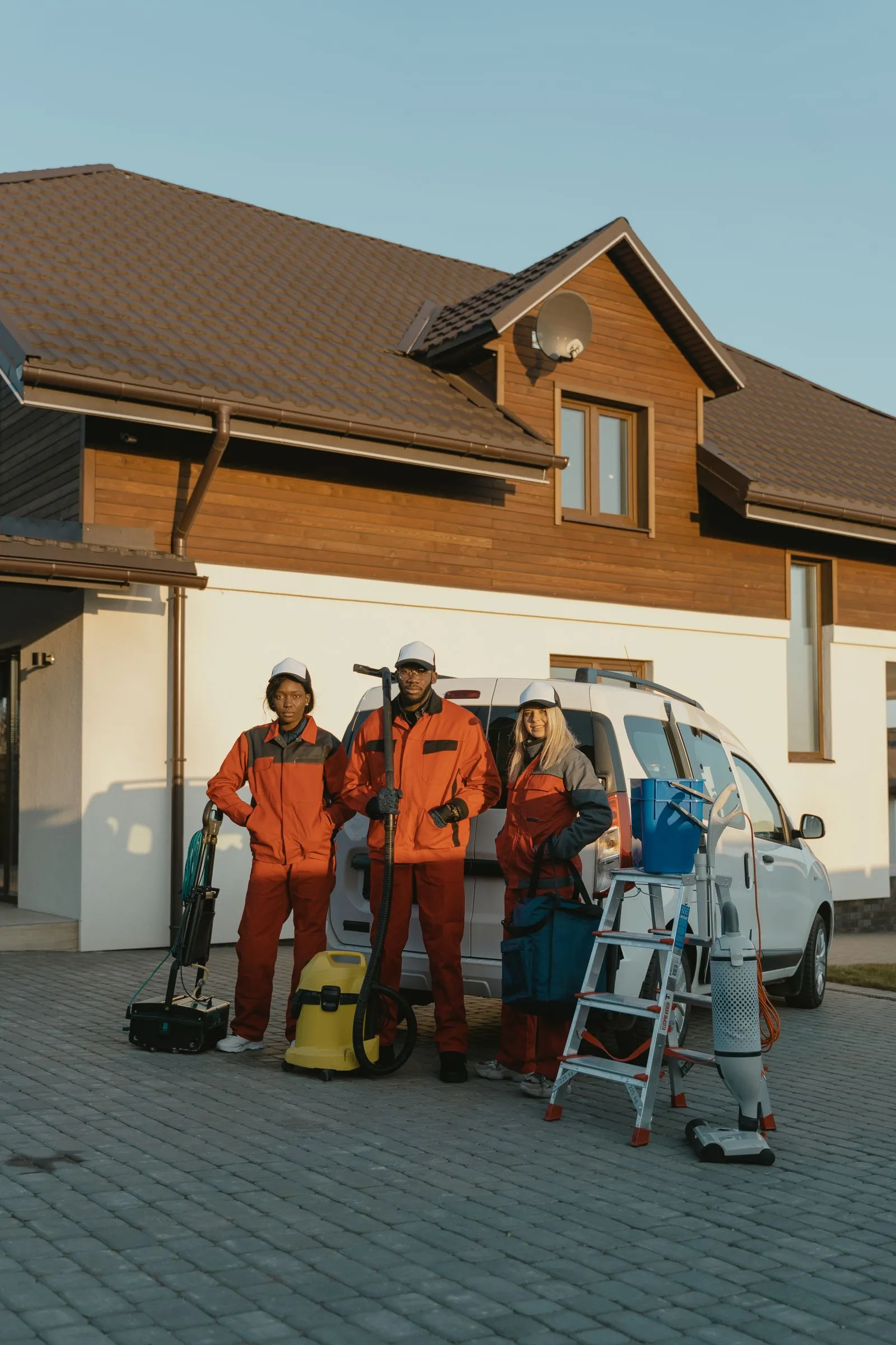 A three-person cleaning crew in uniform outside a house with their equipment